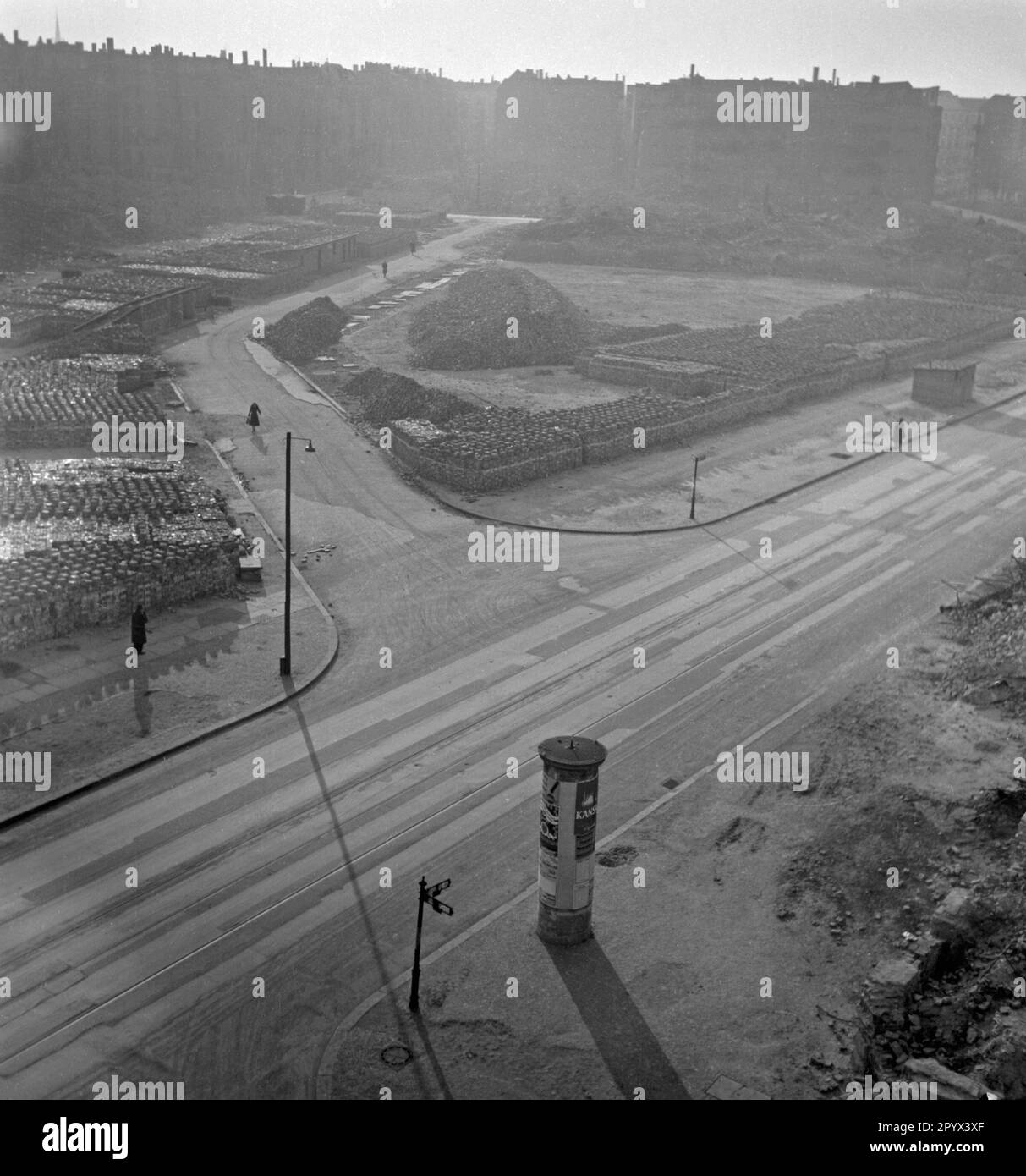 Foto sin fecha de una calle en Berlín, presumiblemente Berlín Occidental, 1950, con áreas abandonadas desordenadas. En el lado izquierdo de la calle, pilas de ladrillos para construir nuevas casas. En primer plano, señales de la calle, linternas y una cartelera enyesada con carteles. En el horizonte, parcialmente destruidos bloques de pisos. Foto de stock