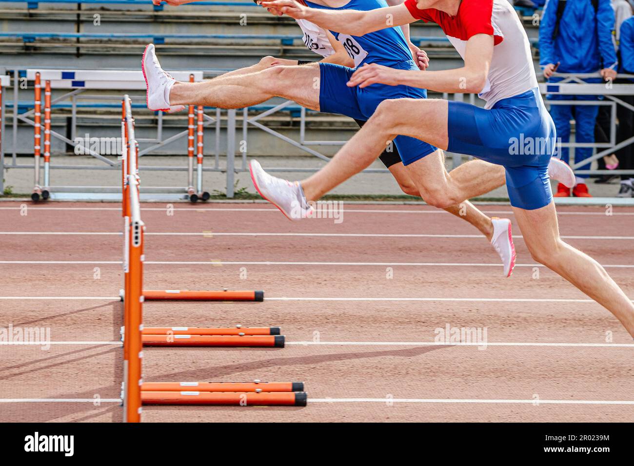 tres corredores masculinos atacan hurdle running 100 metros de carrera en campeonatos de atletismo de verano Foto de stock
