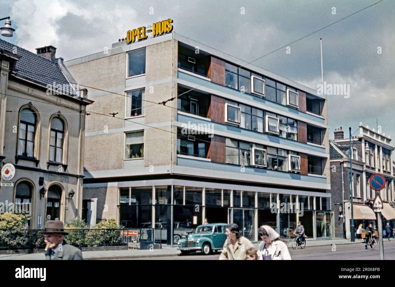 Un moderno edificio de hormigón y ladrillo en el centro de Leiden, Países Bajos en 1959. Alberga un concesionario de automóviles para Opel con un letrero de neón amarillo en la parte superior del bloque que dice “Opel Huis”. Es un desarrollo mixto con tres pisos de apartamentos por encima del espacio comercial de la planta baja. Leiden es una ciudad en la provincia holandesa de Holanda Meridional (Holanda Meridional). Es conocida por su arquitectura centenaria y por la Universidad de Leiden, la más antigua del país, que data de 1575. Esta imagen es de una vieja transparencia amateur. Se verá suave si se utiliza en un tamaño demasiado grande: Una fotografía vintage de 1950s. Foto de stock