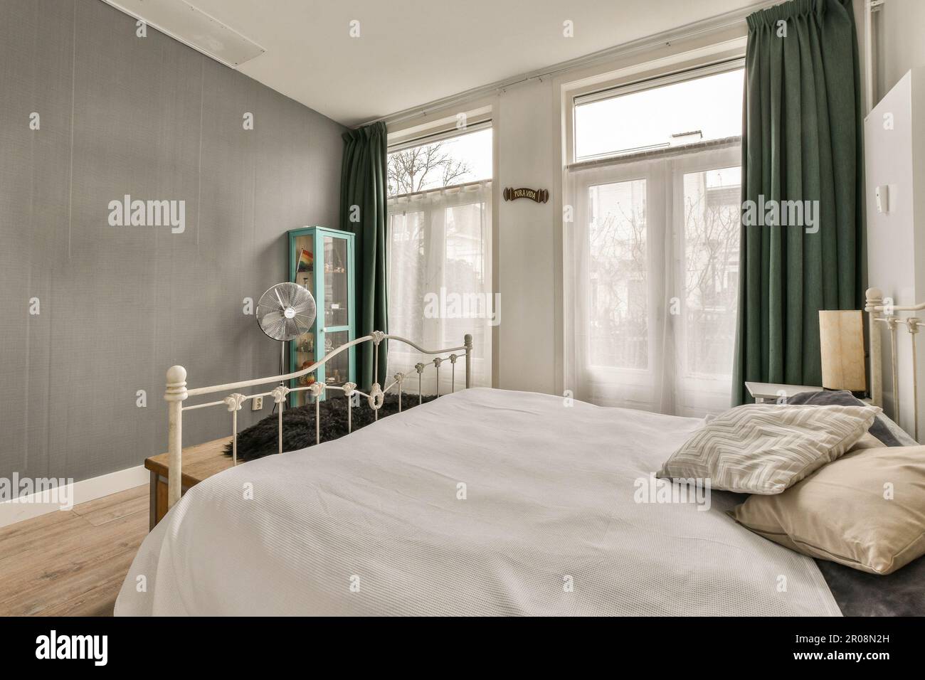 Un dormitorio con paredes blancas y cortinas verdes en los marcos