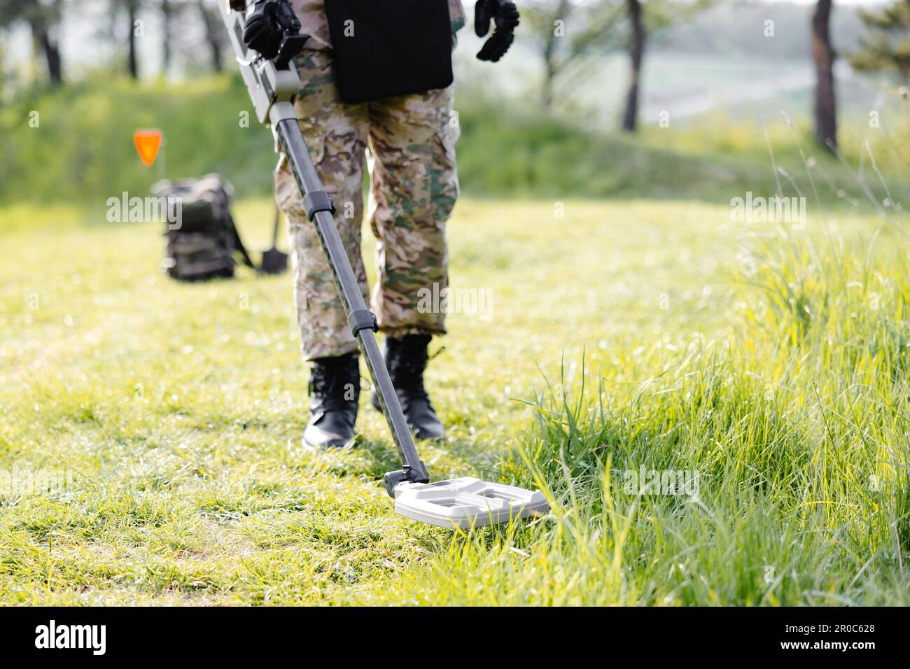 Un hombre con uniforme militar y chaleco antibalas trabaja en el bosque con  un detector de metales.