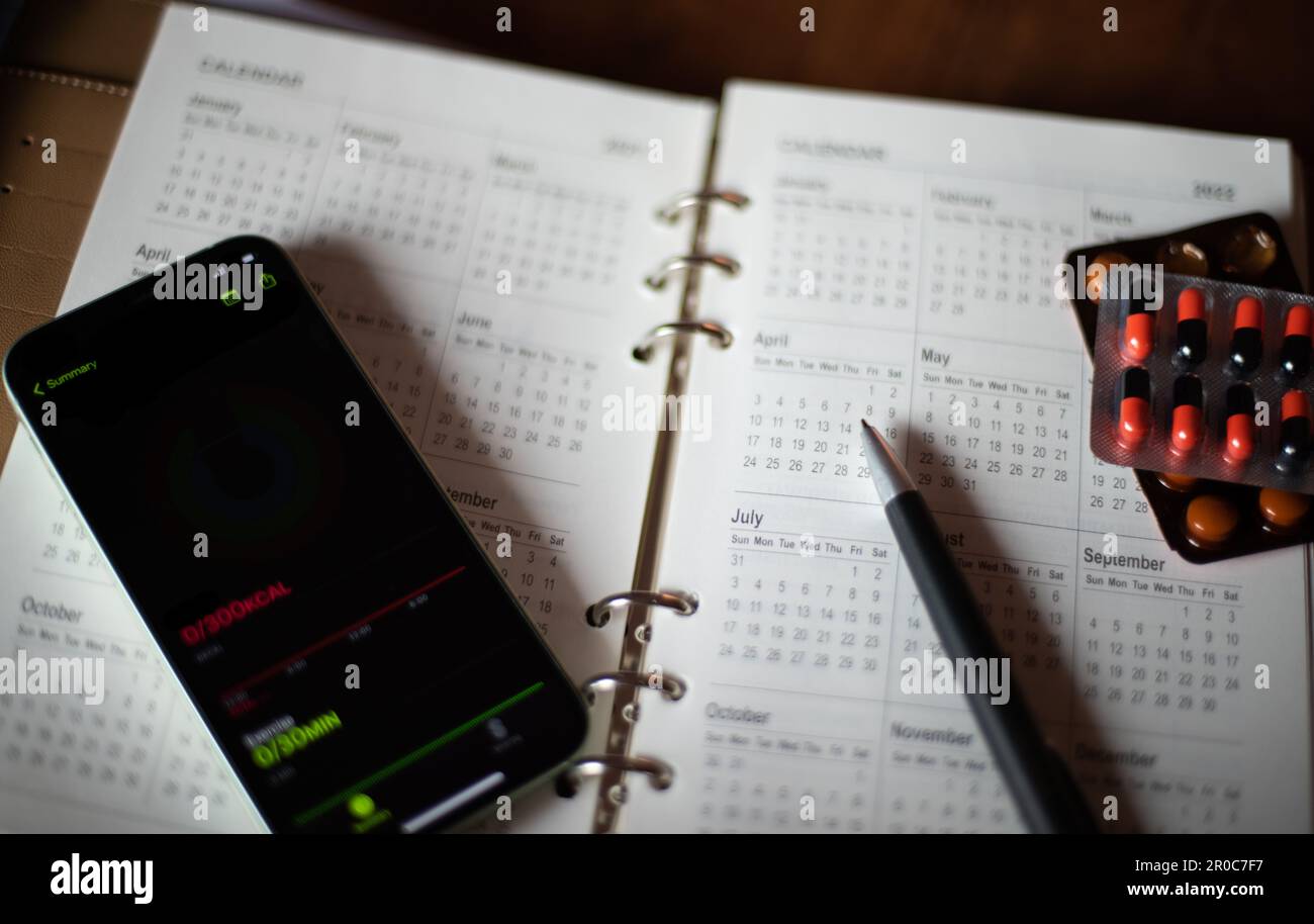 Libro de notas planificador mensual con pluma de medicina y un teléfono móvil con notificación en él Foto de stock