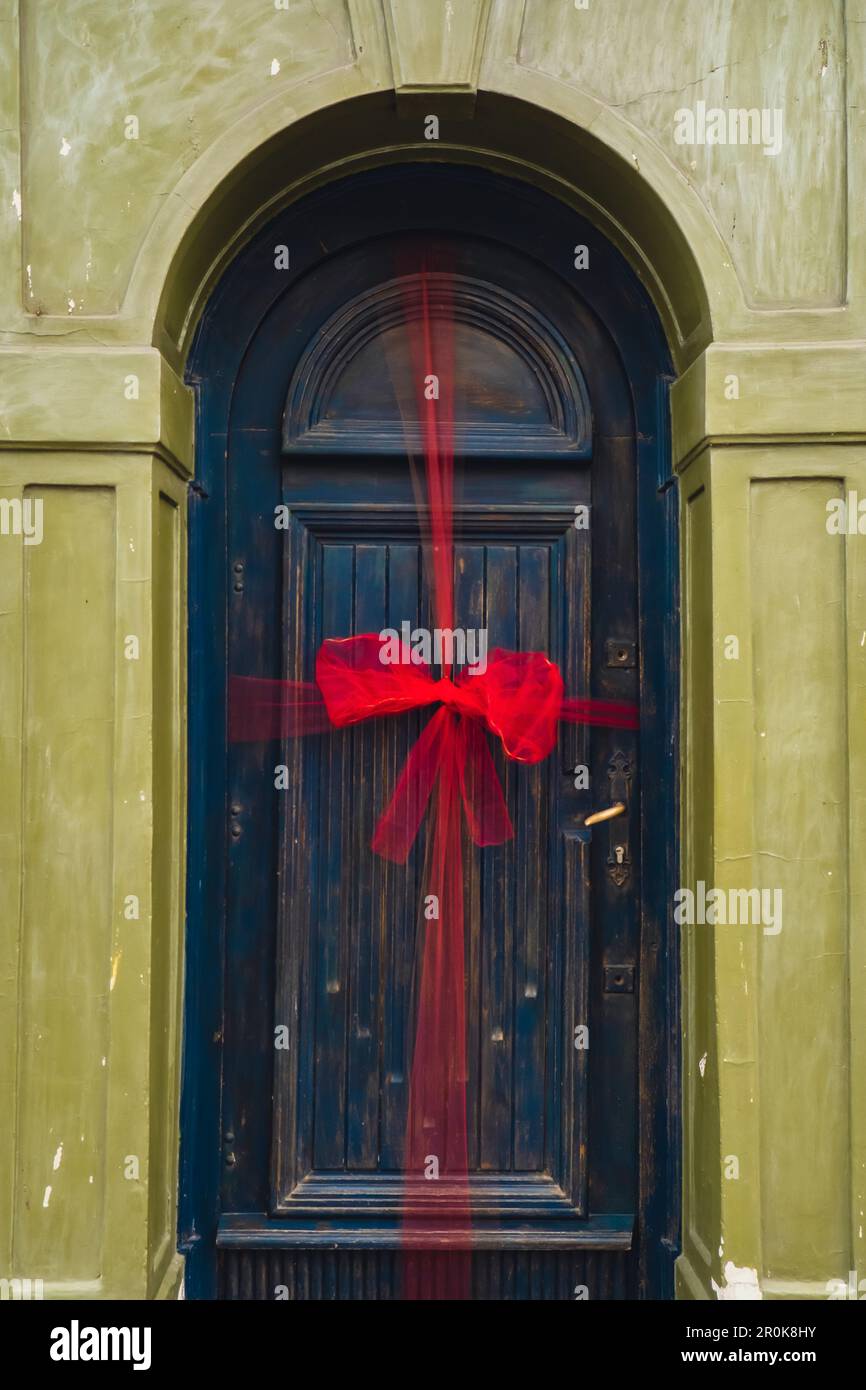 Entrada azul de la puerta principal con lazo de cinta roja de Navidad  atado. Puerta decorada para la temporada de vacaciones. Antigua puerta  rústica vintage. Decoración de vacaciones Bienvenido concepto de casa
