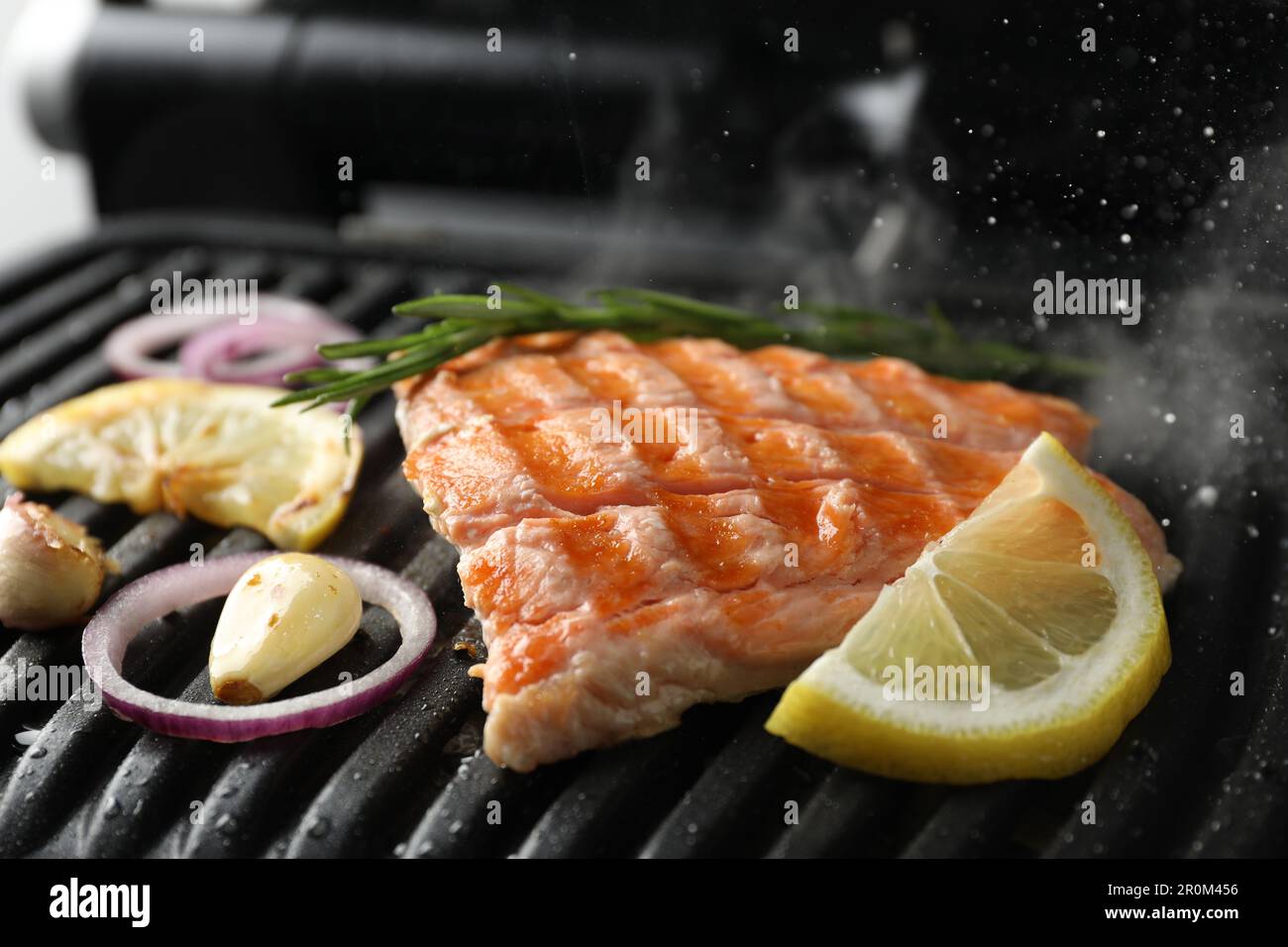 Sabroso salmón cocinando con romero, ajo, cebolla y limón en parrilla  eléctrica, primer plano Fotografía de stock - Alamy