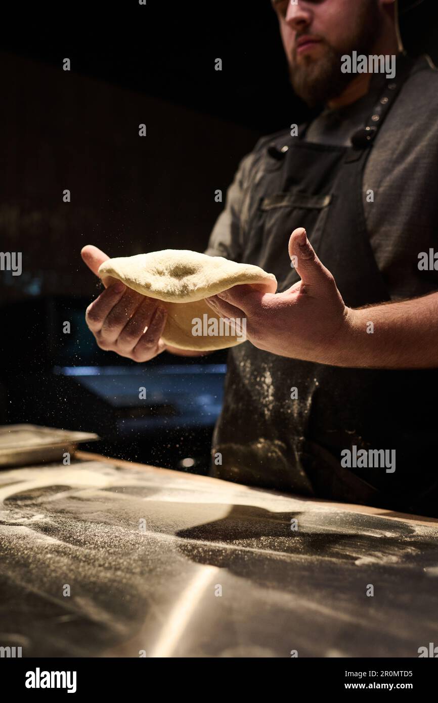 Tiro recortado de joven chef en uniforme sosteniendo pan plano de masa  sobre la mesa mientras prepara pizza para los huéspedes de su propio  restaurante o pizzería Fotografía de stock - Alamy