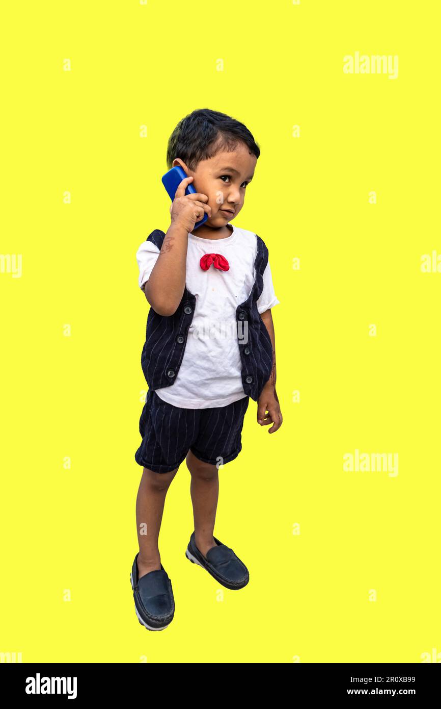 Muchacho con un teléfono móvil, Un pequeño niño bangladesí hablando por teléfono aislado en fondo amarillo con espacio de copia. Foto de stock