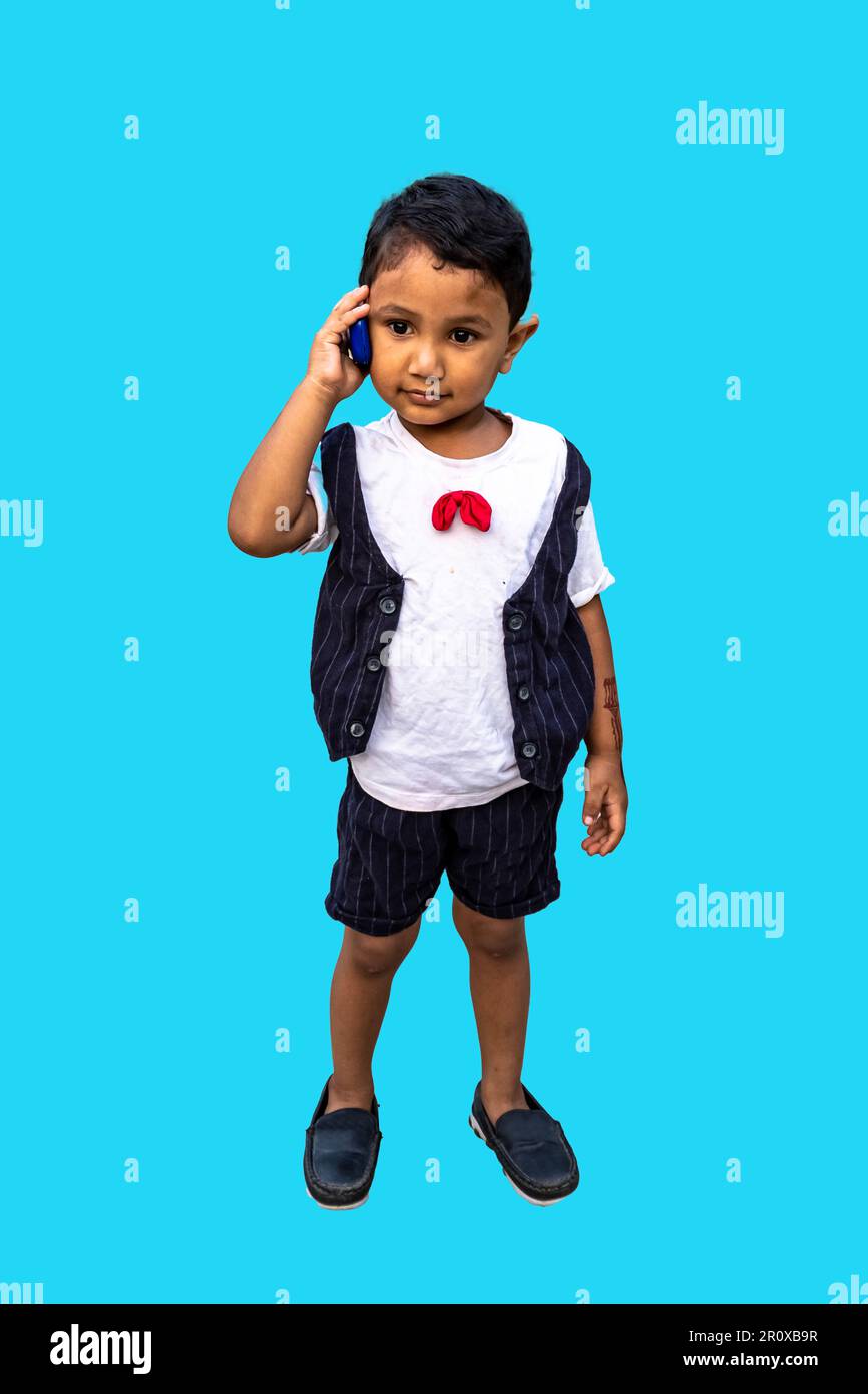 Un niño pequeño en el teléfono, un niño bangladesí hablando por teléfono, aislado en un fondo azul con un espacio para copiar. Foto de stock