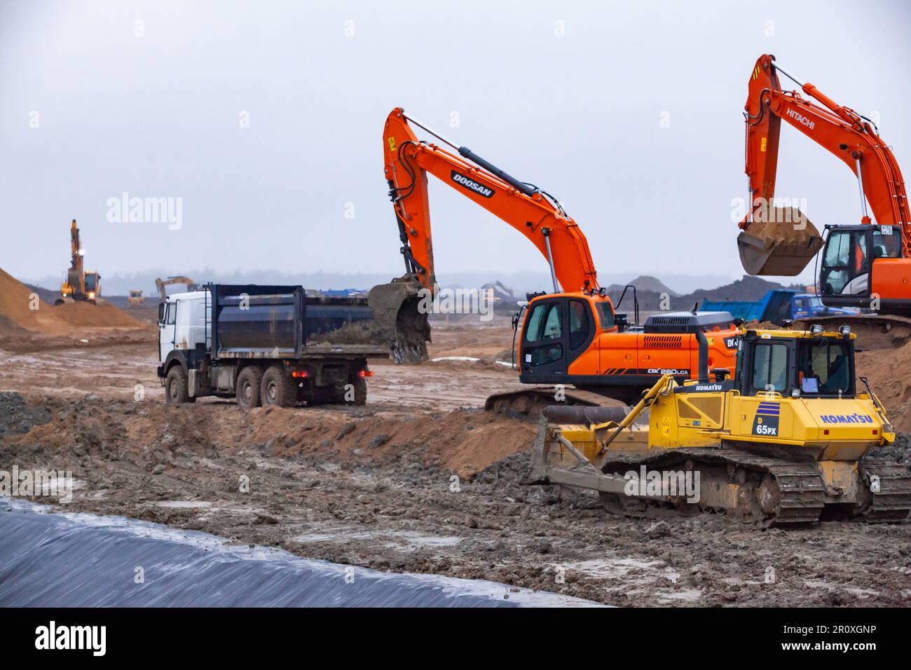 UST-Luga, Óblast de Leningrado, Rusia - 16 de noviembre de 2021: Excavadoras Doosan y Hitachi, topadora Komatsu y camión volquete en obra. Día lluvioso, d Foto de stock