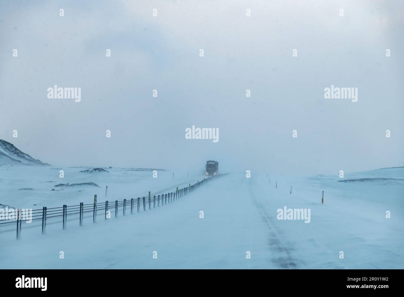 Vista en perspectiva del conductor sobre la carretera principal en Islandia durante una tormenta de nieve con la carretera cubierta de nieve y poca visibilidad con un gran camión que se aproxima Foto de stock