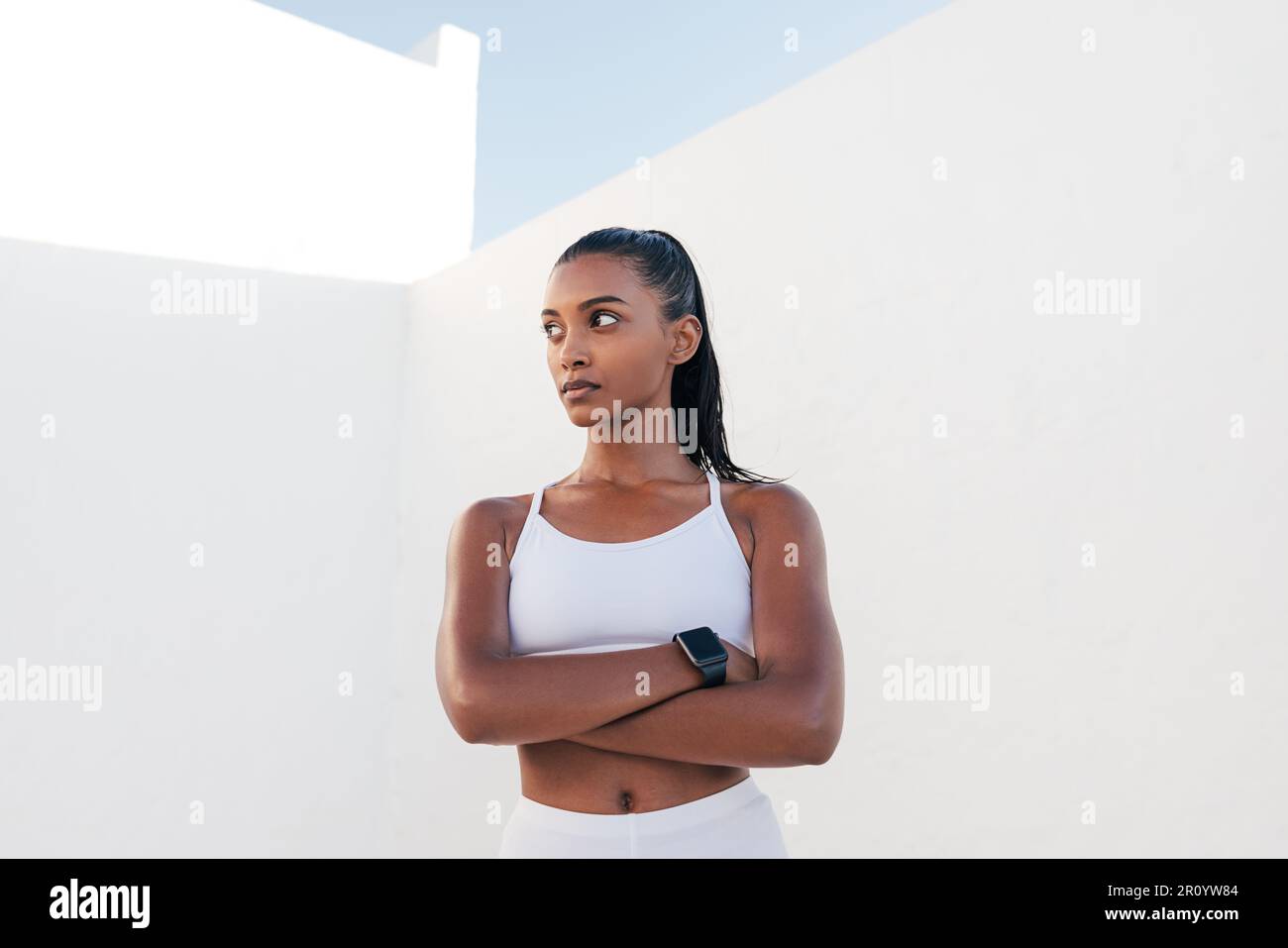 Influyente de fitness fuerte y confiado. Mujer en ropa deportiva blanca con las manos cruzadas. Foto de stock