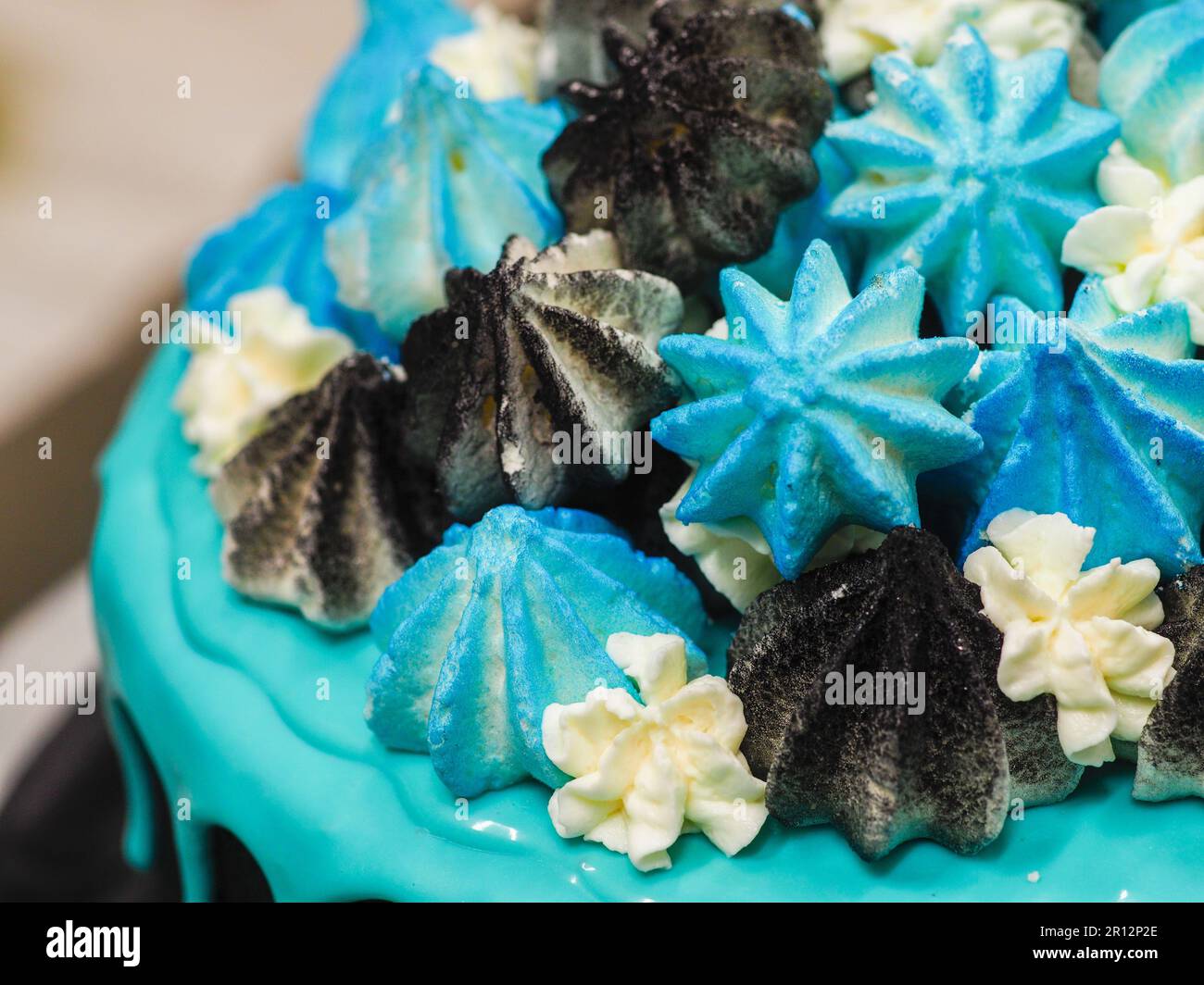 Un primer plano de un delicioso pastel negro decorado con escarcha azul y merengues de colores Foto de stock