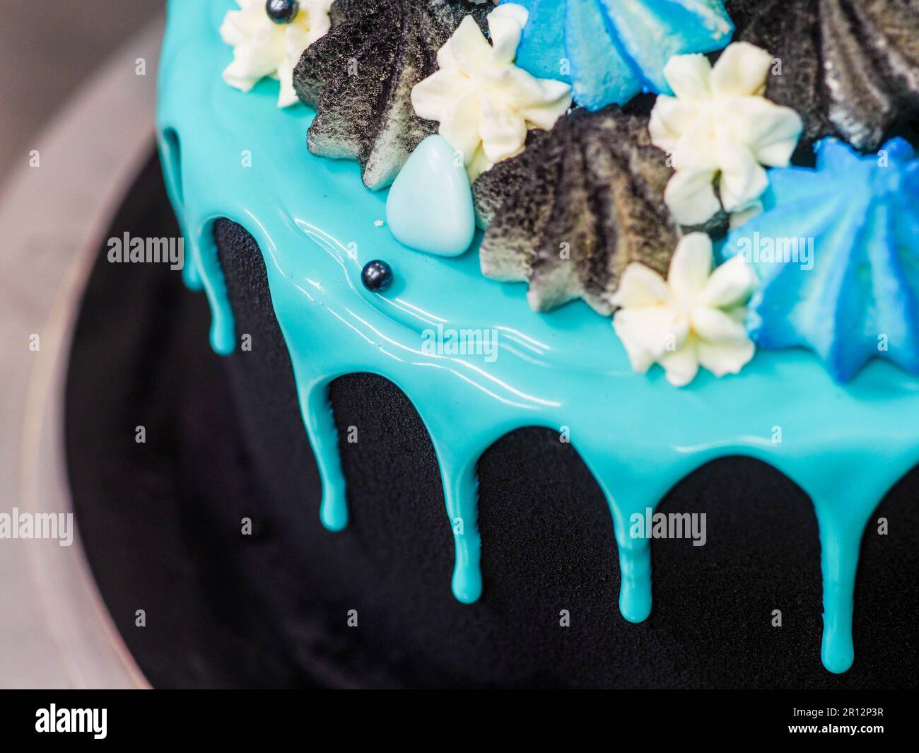 Un primer plano de un delicioso pastel negro decorado con escarcha azul y merengues de colores Foto de stock