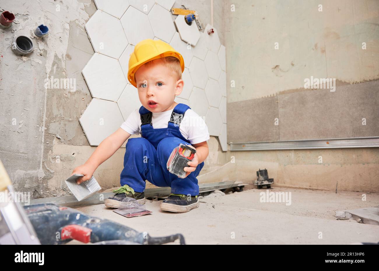 El Chico Imita Al Trabajador. Niño En Mono De Trabajo Y Casco Con