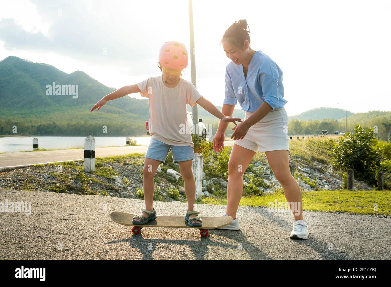 Madre enseñando a su hija a patinar en el parque. Niño montando tabla de skate. Deportes saludables y actividades al aire libre para niños en edad escolar Foto de stock