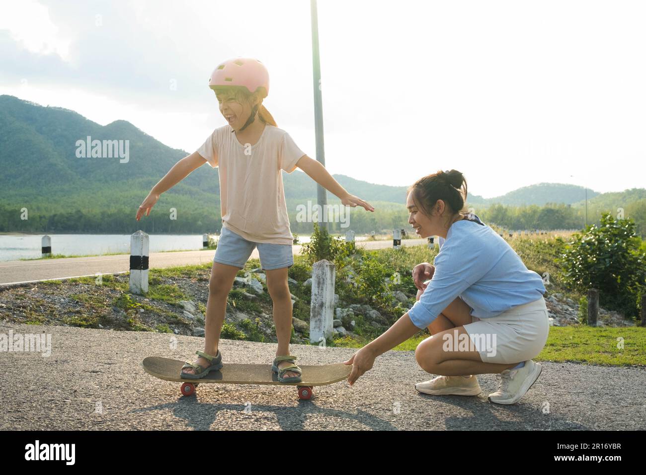 Madre enseñando a su hija a patinar en el parque. Niño montando tabla de skate. Deportes saludables y actividades al aire libre para niños en edad escolar Foto de stock