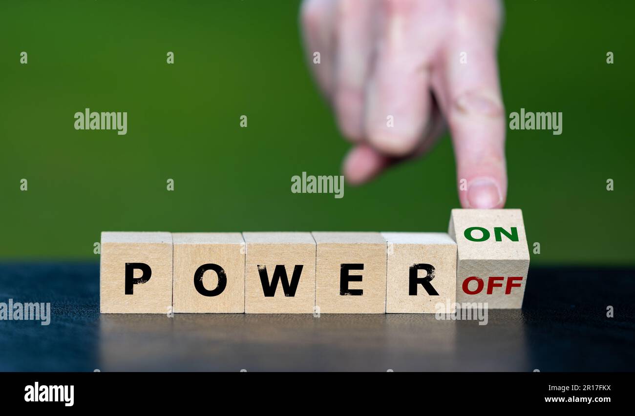 La mano gira el cubo de madera y cambia la expresión 'power off' a 'power on'. Foto de stock