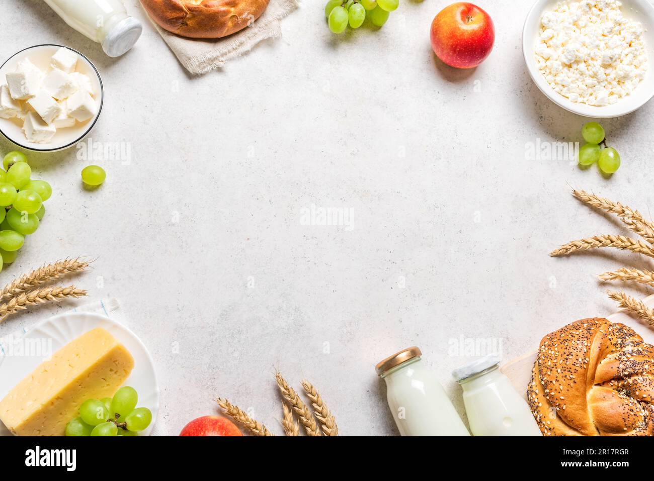 Shavuot feliz - marco religioso del concepto del día de fiesta judío con los productos lácteos, el queso, el pan tradicional, las botellas de leche, el trigo y las frutas en madera blanca Foto de stock