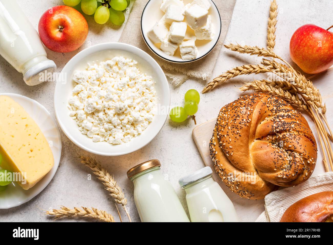 Concepto de Shavuot de vacaciones judías con productos lácteos, queso, pan, botellas de leche, trigo y uvas de cerca, colocación plana. Foto de stock