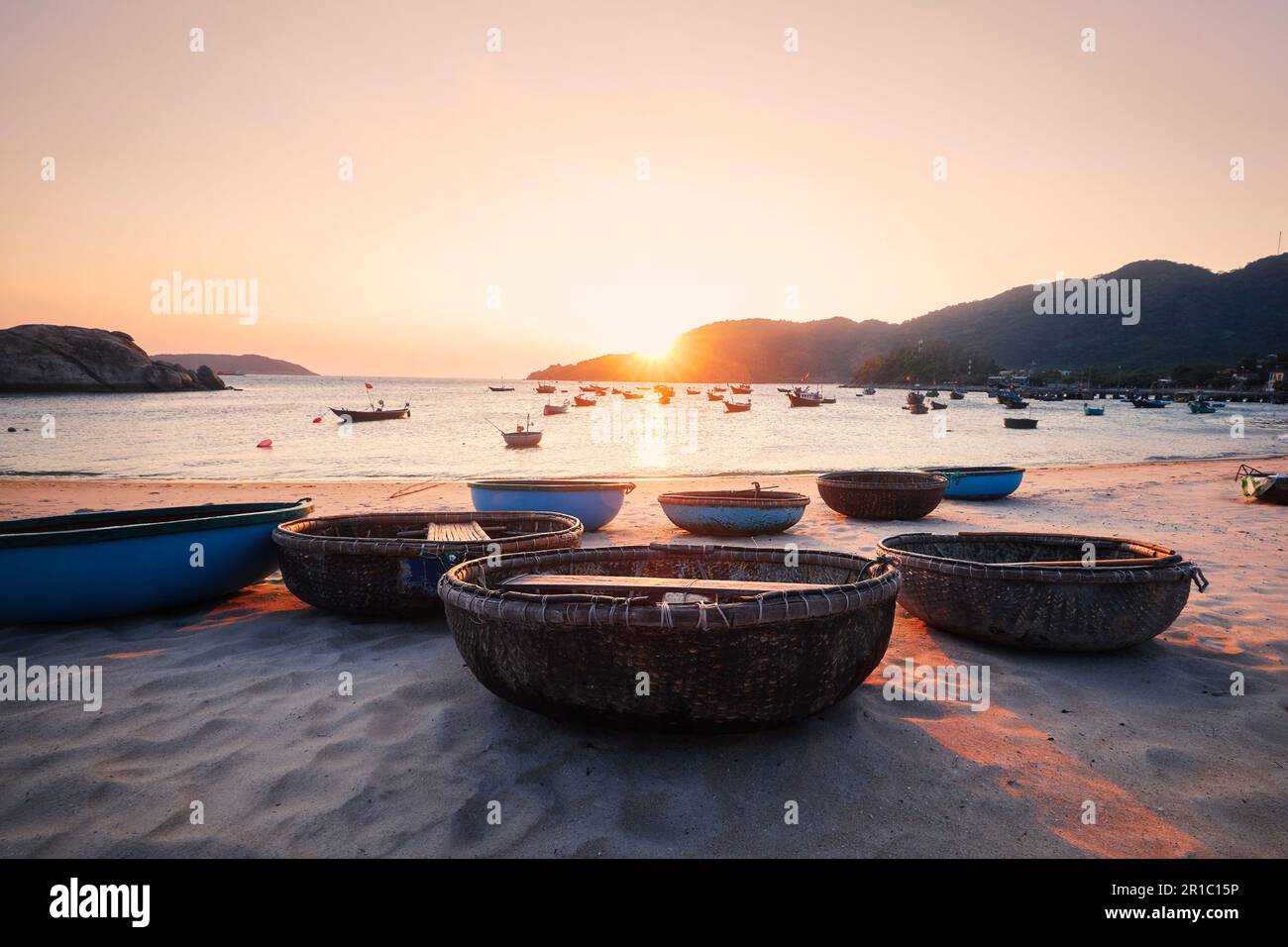 Barcos de la cesta en la playa de arena en la bahía contra el mar en la puesta del sol hermosa. Pueblo pesquero en las islas Cham en Vietnam. Foto de stock
