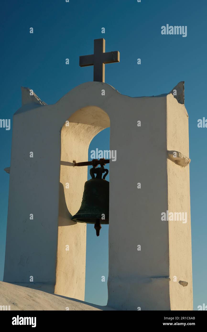 Vista de una cruz religiosa y una campana en la parte superior de una antigua iglesia ortodoxa griega encalada en Ios Grecia Foto de stock