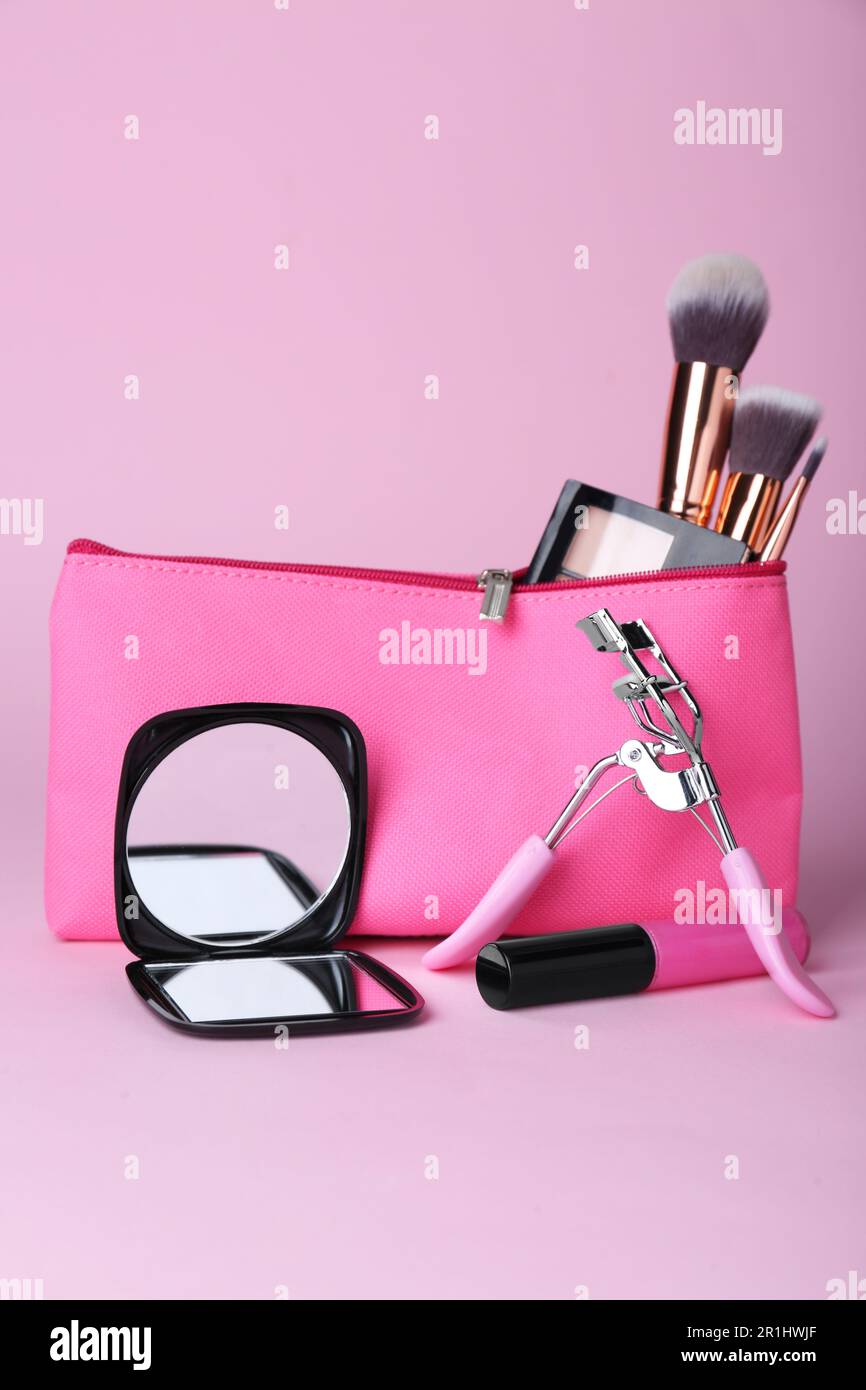 Elegante espejo de bolsillo y bolso cosmético con productos de maquillaje sobre fondo violeta Foto de stock