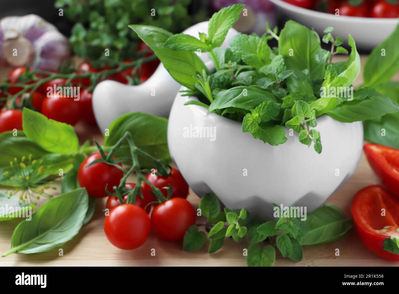 Mortero con hierbas frescas, pimienta y tomates cherry en la mesa de madera, primer plano Foto de stock