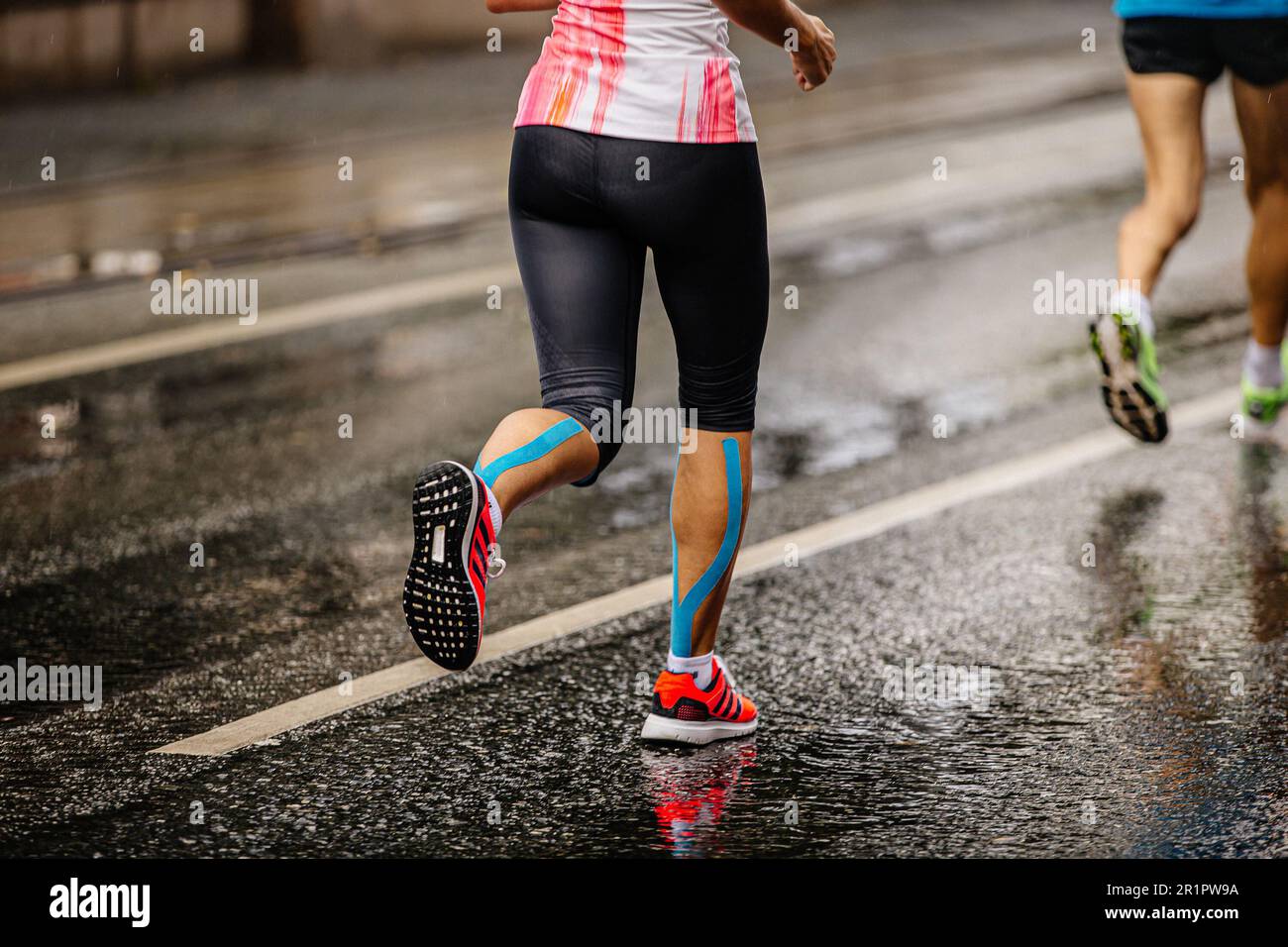 Piernas zapatillas de running mujer Adidas running maratón carrera en  carretera mojada, cinta de kinesio en espinillas Fotografía de stock - Alamy