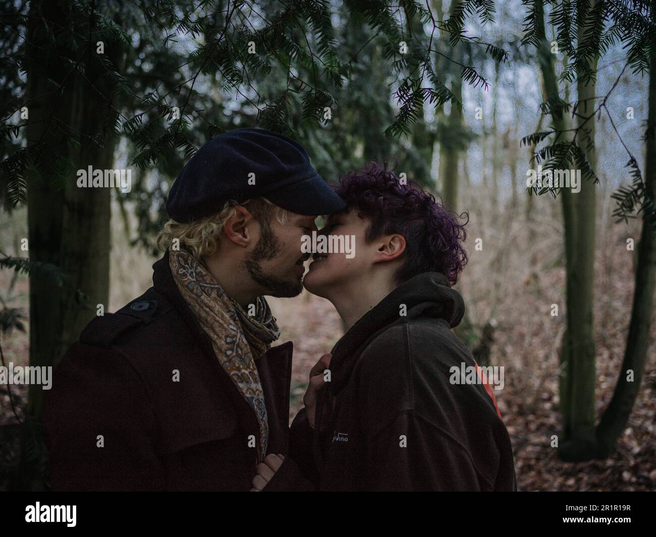 Pareja no binaria besándose en el bosque Foto de stock