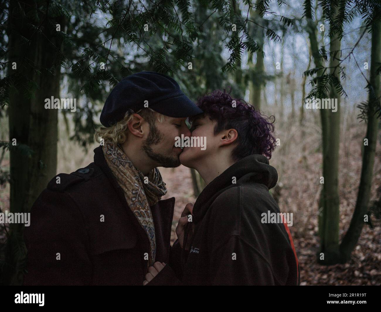 Pareja no binaria besándose en el bosque Foto de stock