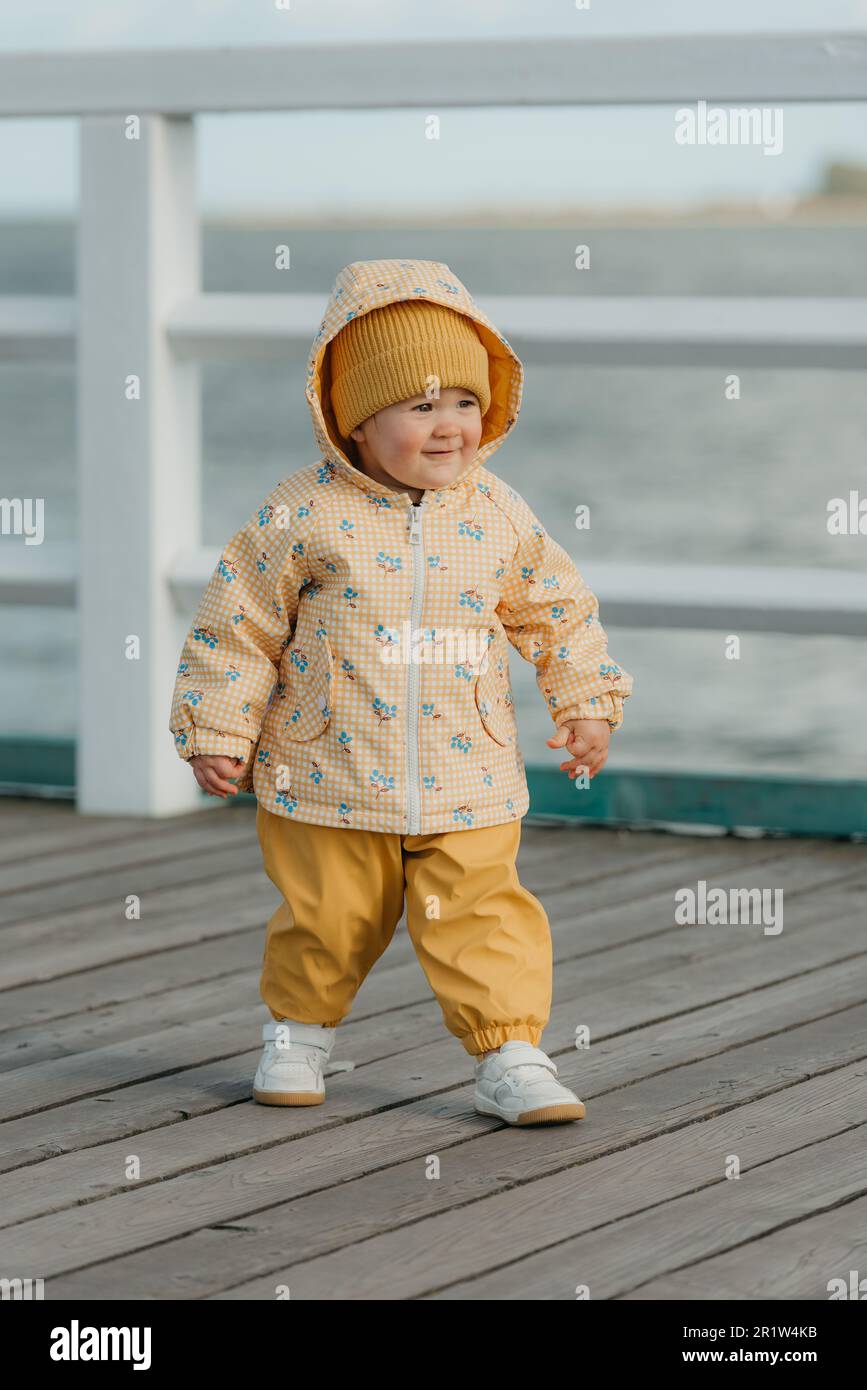 Un niño pequeño con una chaqueta amarilla y pantalones camina en el muelle  Fotografía de stock - Alamy