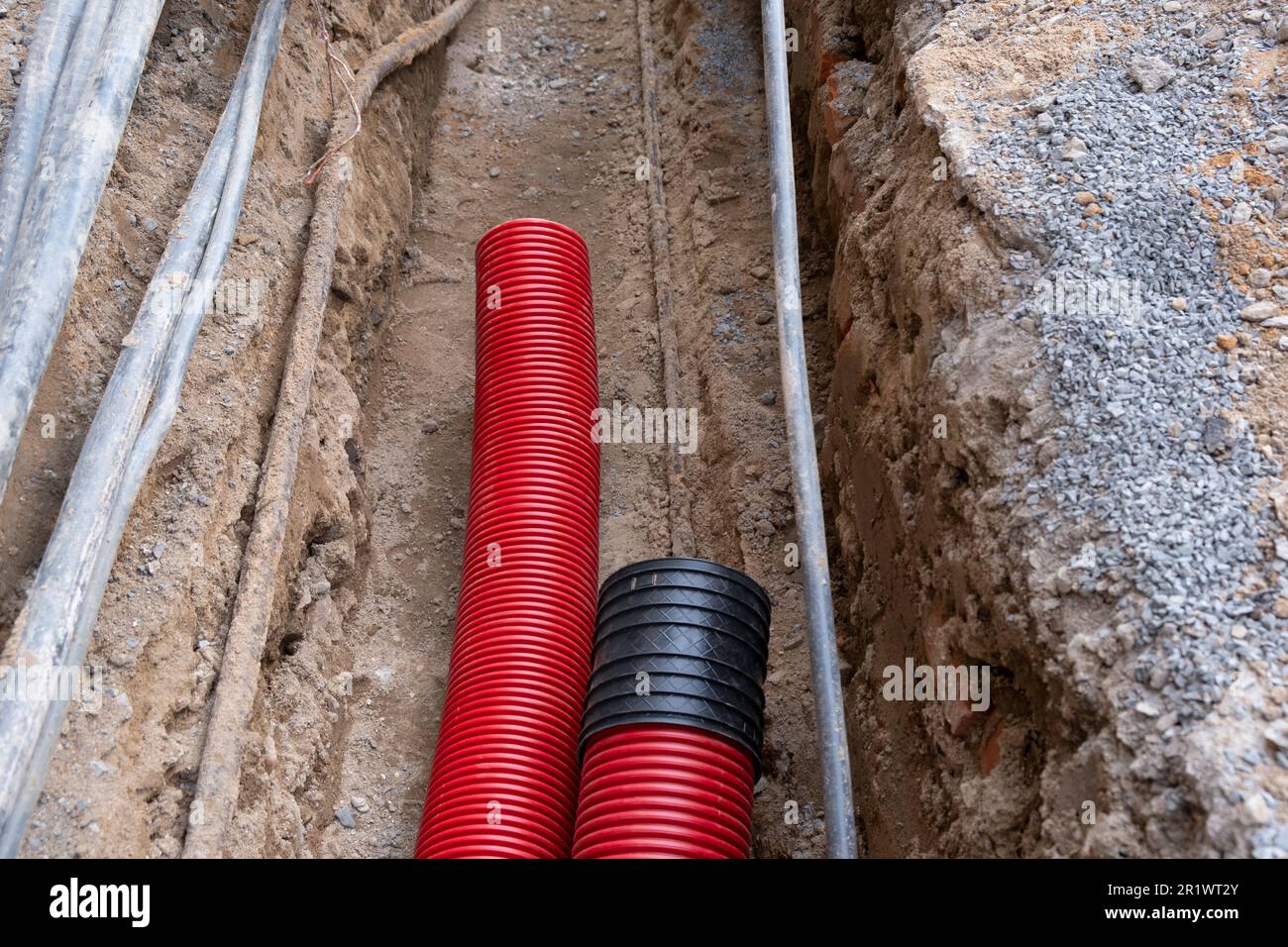 El tubo corrugado rojo está enterrado bajo tierra en la calle hecho para la  instalación de infraestructura de cable eléctrico. Sitio de construcción  con Una gran cantidad de suministro e Fotografía de
