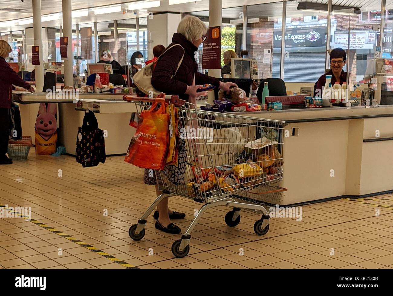 Fotografía de un trabajador de Sainsbury's vestido con una cara cubierta durante la pandemia de COVID-19. Se instalaron escudos de plástico para ayudar a proteger aún más al personal. Foto de stock