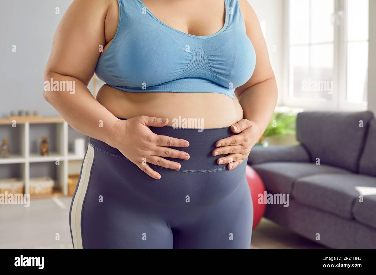 Mujer obesa con sobrepeso en sujetador deportivo y leggings sosteniendo sus  manos sobre su vientre gordo Fotografía de stock - Alamy