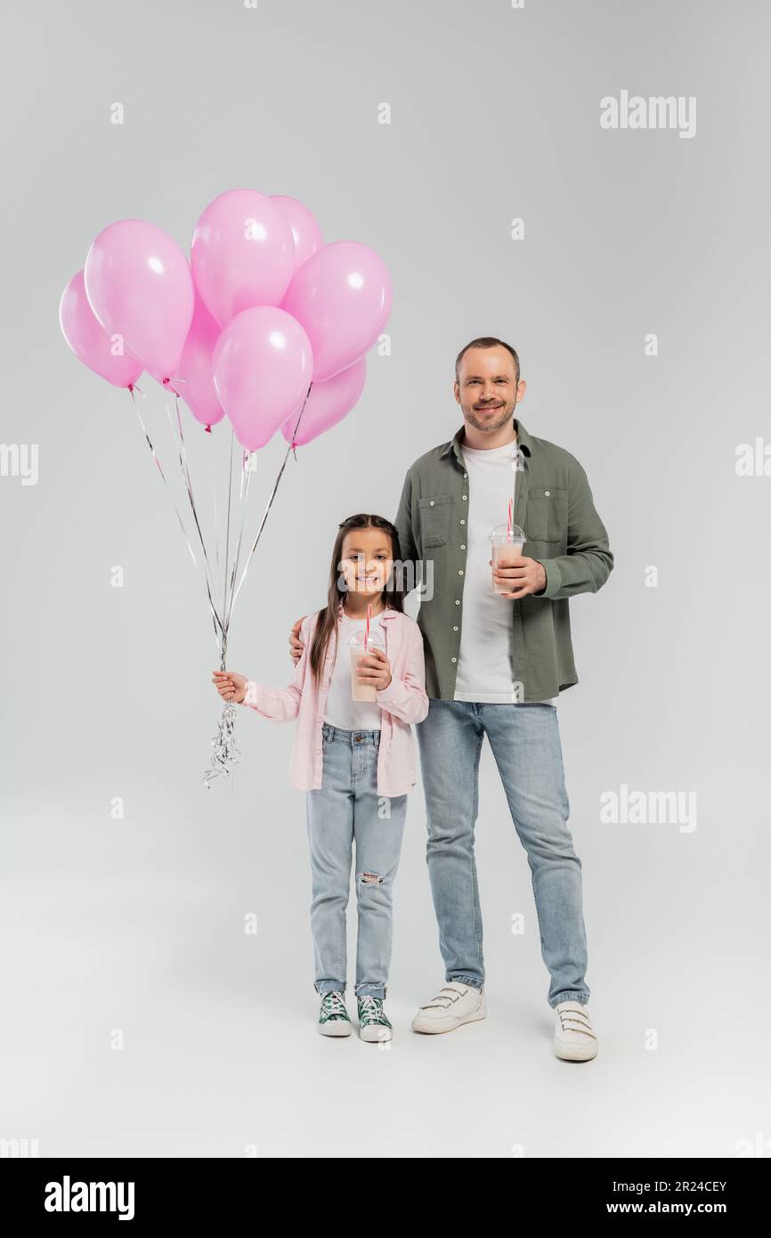 Padre sonriente e hija preadolescente en ropa casual sosteniendo batidos y  globos rosados mientras celebra el día de protección infantil y de pie en  gris Fotografía de stock - Alamy
