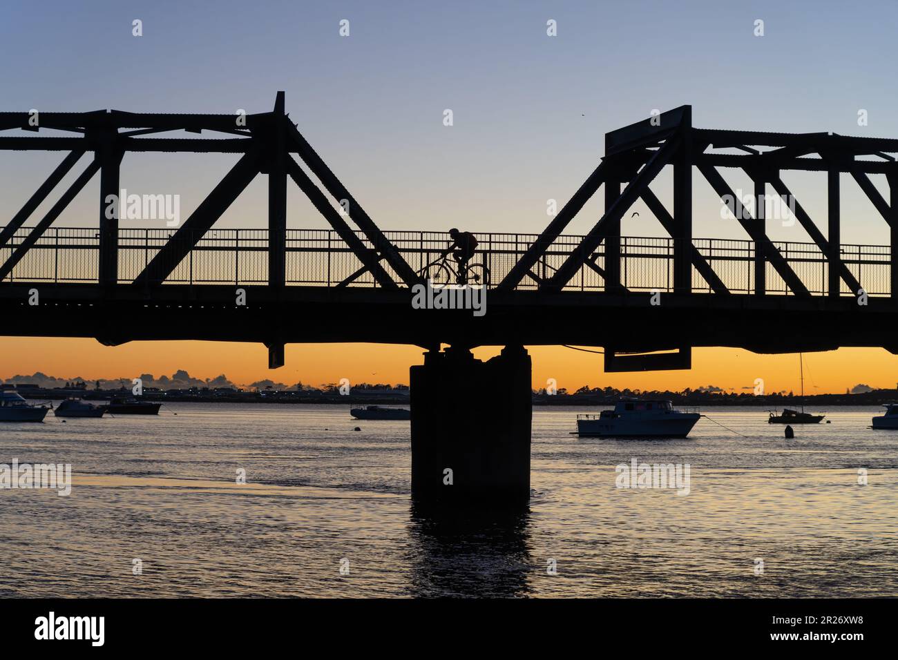 En silueta irreconocible ciclista retroiluminado en el amanecer montando a través del puente del ferrocarril de Tauranga, Nueva Zelanda. Foto de stock