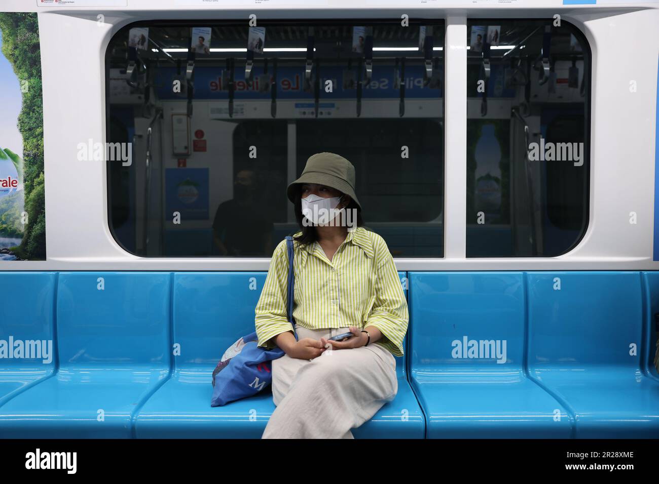 Mujer indonesia joven con una máscara en un vagón vacío de Mass Rapid Transit con el anuncio de Le Minerale exhibido sobre su cabeza en Yakarta, Indonesia Foto de stock