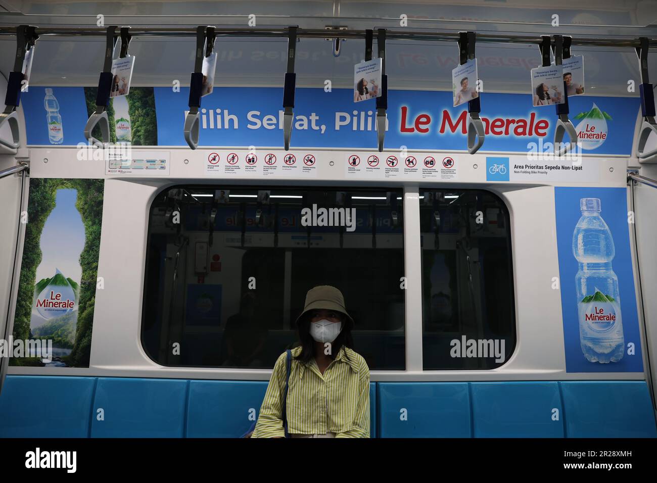Mujer indonesia joven con una máscara en un vagón vacío de Mass Rapid Transit con el anuncio de Le Minerale exhibido sobre su cabeza en Yakarta, Indonesia Foto de stock