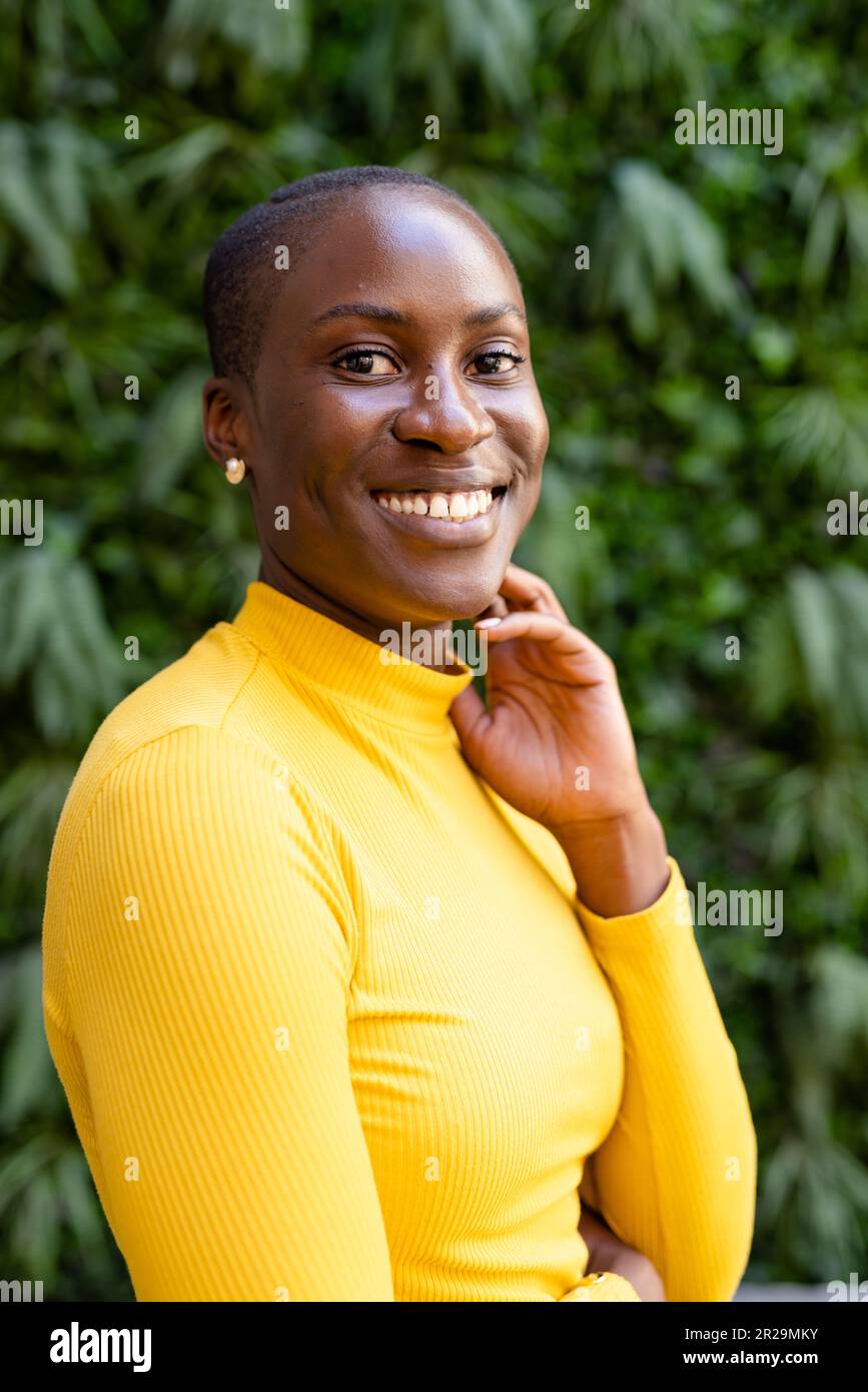 Retrato de sonriente empresaria afroamericana con el pelo corto posando contra las plantas Foto de stock