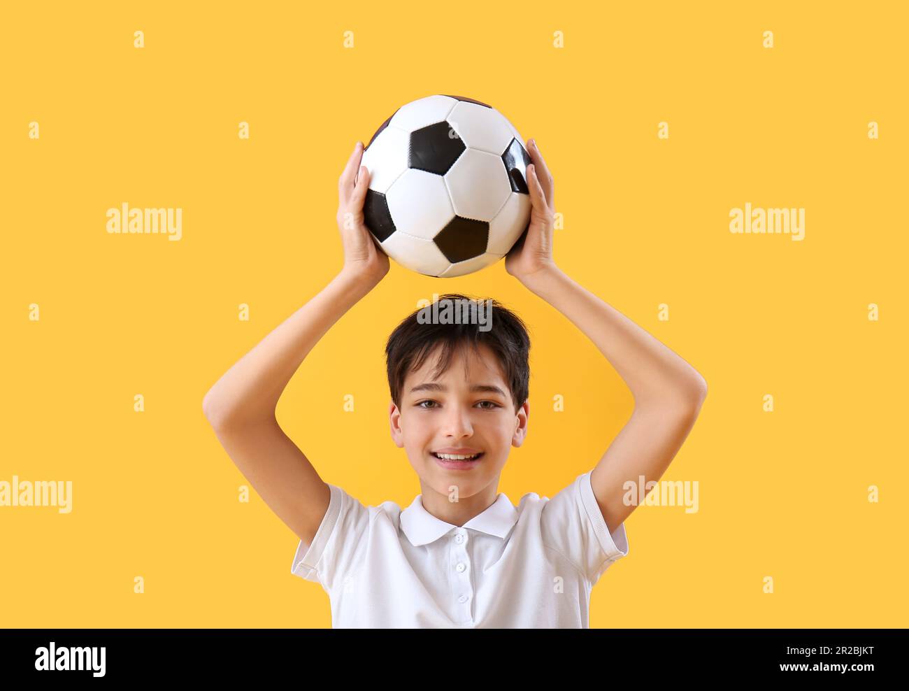 Niño pequeño con la pelota de fútbol sobre fondo amarillo