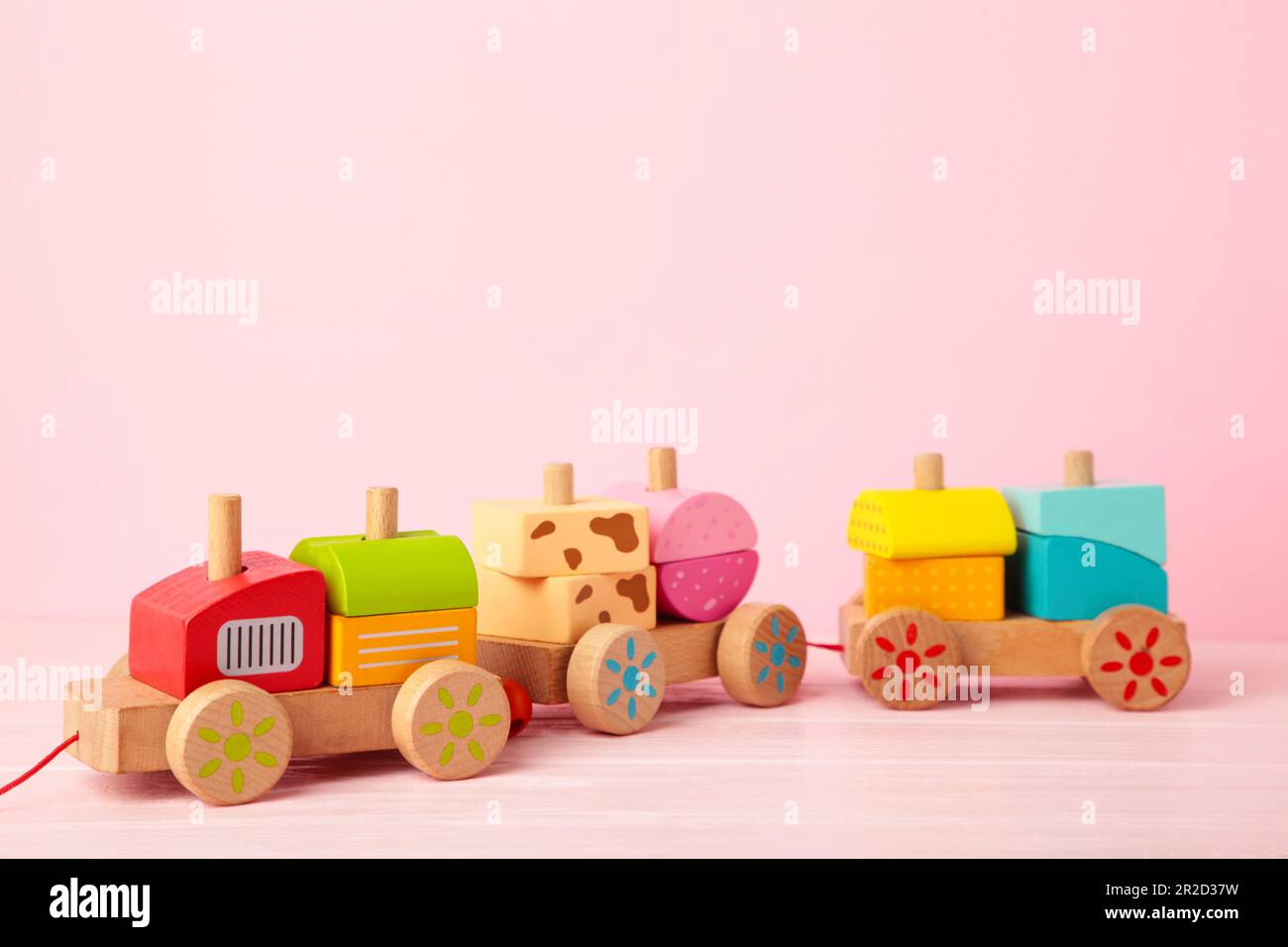 Apilamiento del juguete del niño del tren para los niños pequeños en el fondo rosado con la reflexión de la sombra. Tren de bebé hecho de bloques geométricos de madera. Madera colorida Foto de stock