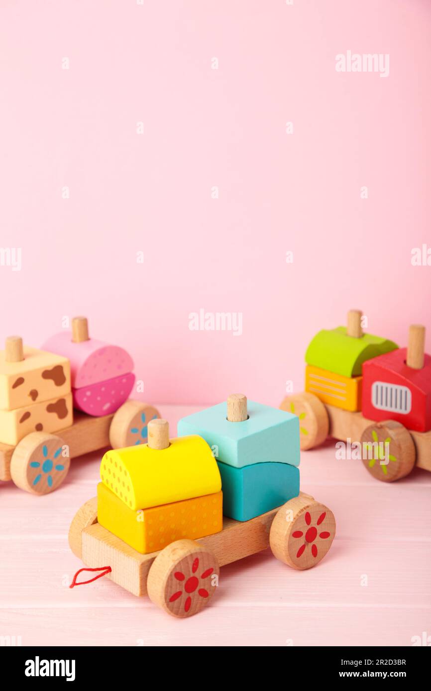 Apilamiento del juguete del niño del tren para los niños pequeños en el fondo rosado con la reflexión de la sombra. Tren de bebé hecho de bloques geométricos de madera. Madera colorida Foto de stock