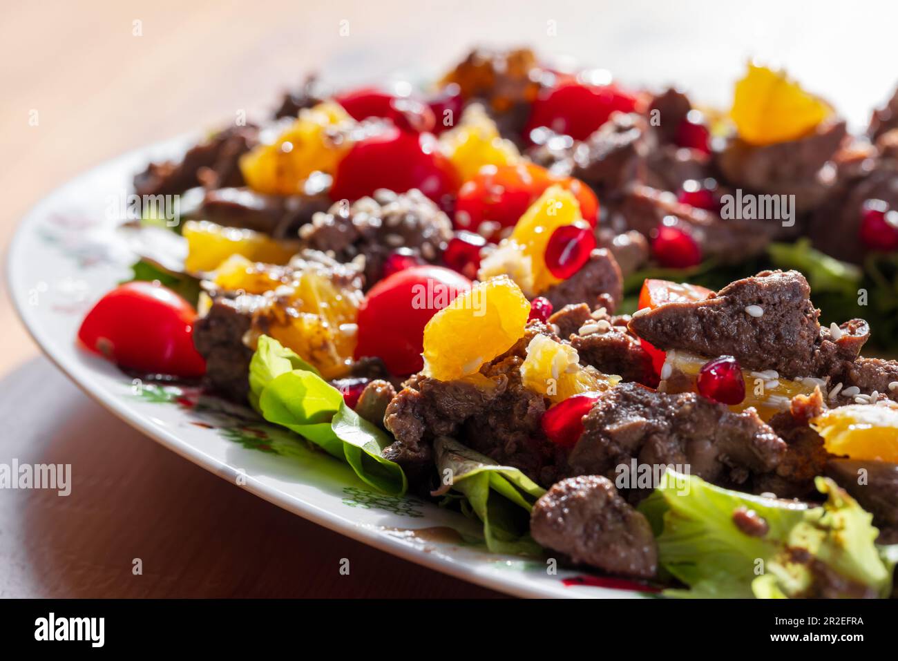 Foto de cerca de ensalada caliente con hígado de pollo, tomates cherry, naranja, lechuga, semillas de granada y sésamo Foto de stock