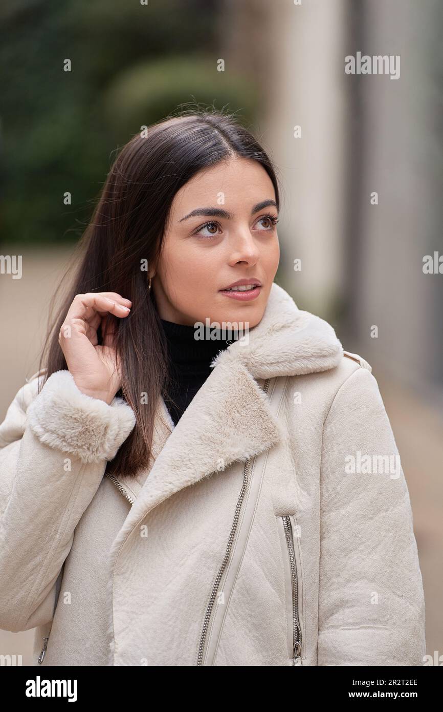 retrato de la mujer morena hermosa posando sosteniendo su pelo con su mano  con la chaqueta blanca en la ciudad Fotografía de stock - Alamy