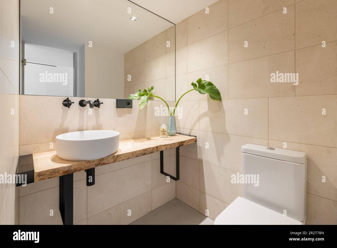 Elegante cuarto de baño luminoso con azulejos de color beige en las paredes  y un gran espejo con un lavabo en una encimera de madera y un inodoro. El  concepto de lo