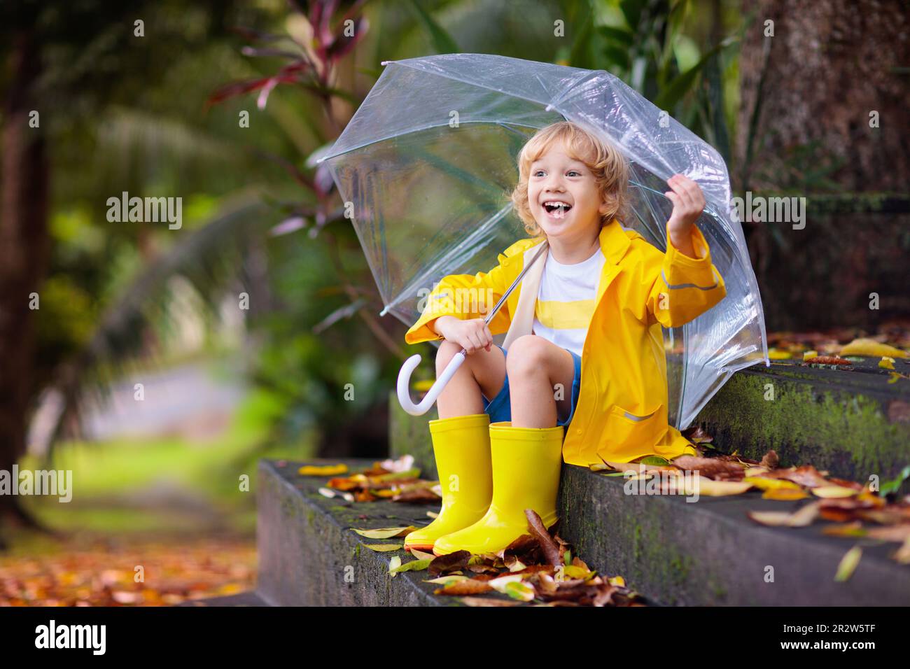 Niño Jugando Bajo La Lluvia De Otoño. Niño Con Paraguas. Niño Corriendo En  Un Parque En Temporada De Otoño. Diversión Al Aire Libre Para Niños En  Cualquier Clima. Ropa Impermeable Para La