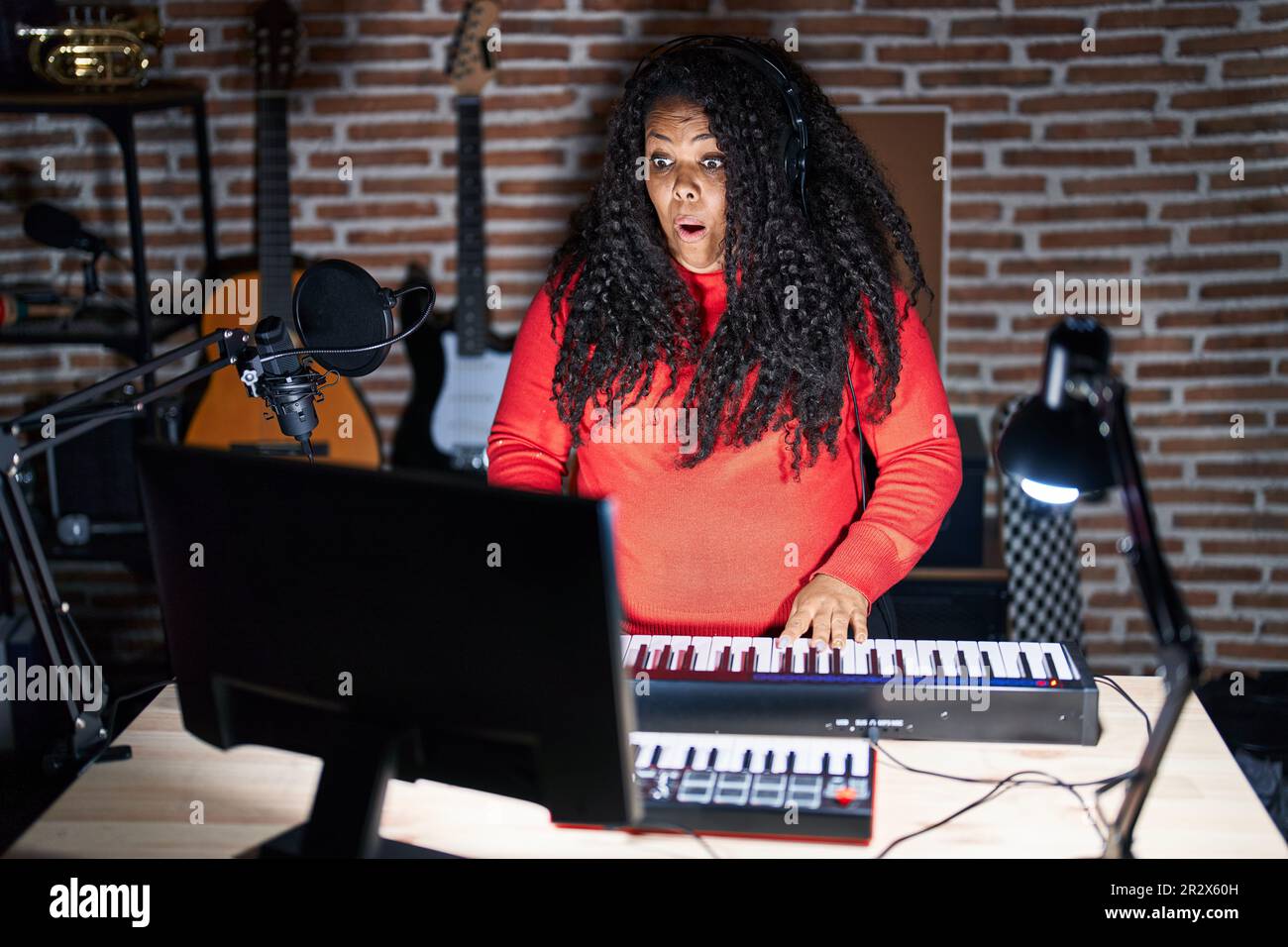 Mujer hispana que toca el piano en el estudio de música asustada y  conmocionada con la expresión sorpresa, el miedo y la cara emocionada  Fotografía de stock - Alamy