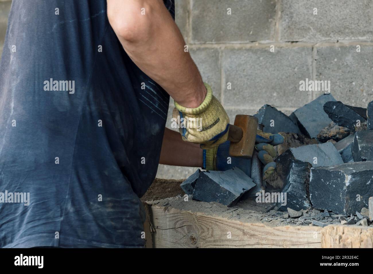 Hombre trabajando con piedra dura con martillo y cincel. Stone emason divide las piedras de basalto Foto de stock