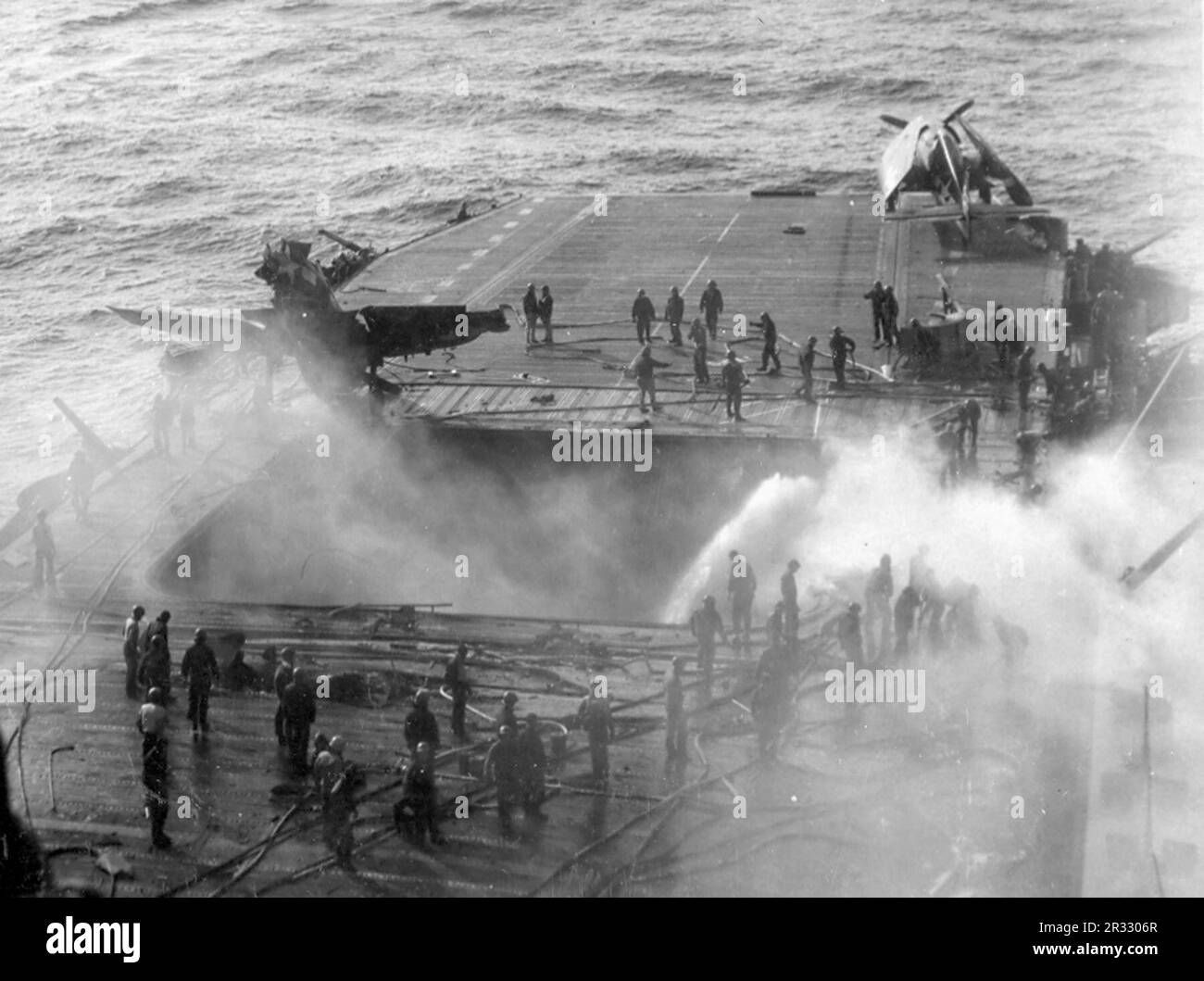 La tripulación de los Estados Unidos El portaaviones USS Enterprise (CV-6) combatió incendios después de que un kamikaze golpeara el ascensor delantero el 14 de mayo de 1945. Cuando Japón se enfrentaba a la derrota a finales de 1944, decidió destruir barcos estadounidenses con bombas suicidas, conocidas como Kamikaze. Estos ataques eran un arma física y psicológica potente y hundieron un total de 47 barcos a un costo de más de 3000 pilotos y aviones. A finales de 1944 la Marina de los Estados Unidos era lo suficientemente grande como para que las pérdidas fueran insignificantes y no alteraran el curso de la guerra. Foto de stock