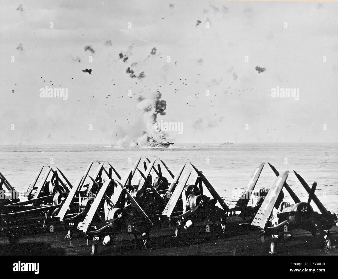 Estados Unidos El portaaviones de la Armada USS Enterprise (CV-6) en llamas después de que el barco fuera alcanzado por un kamikaze frente a Kyushu en el 14 de mayo de 1945. El elevador delantero, que pesa muchas toneladas, se puede ver arrojado por la explosión. La foto fue tomada de USS Essex (CV-9). Vought F4U-1 Corsarios del Escuadrón de Bombardeo de Combate 83 (VBF-83) son visibles en primer plano. Foto de stock