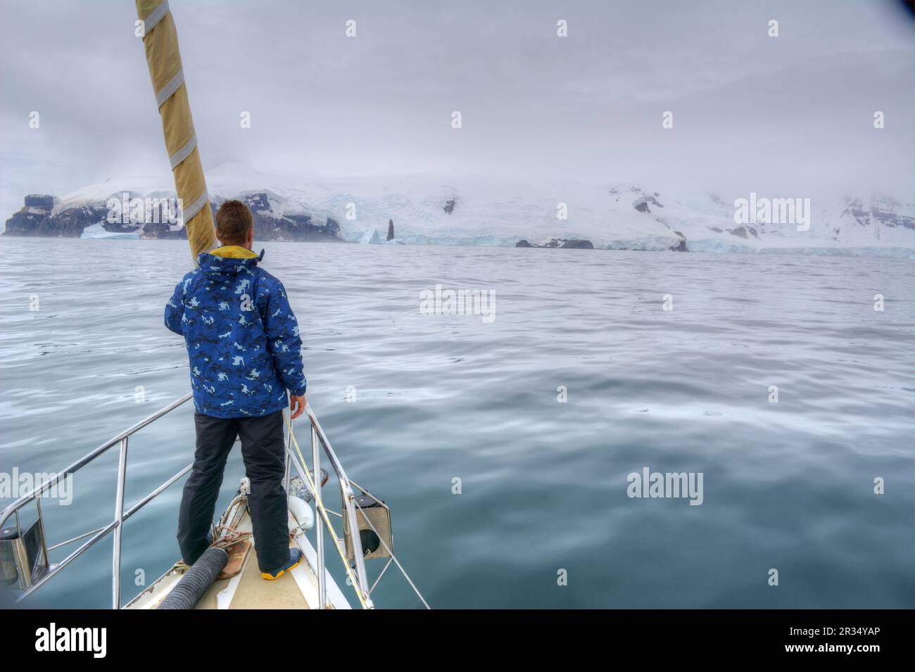 Un hombre viajero se encuentra en la proa de un yate de vela con destino a la Antártida Foto de stock